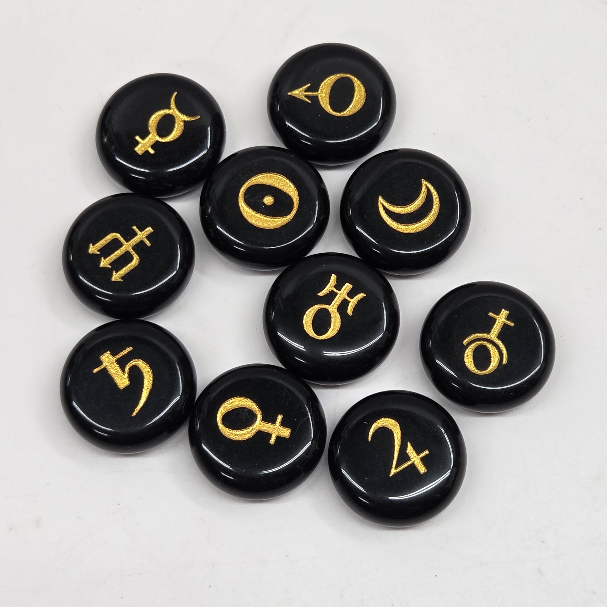 Nine round black stone pendants with gold celestial and astrological symbols, arranged in a cluster on a light gray background.
