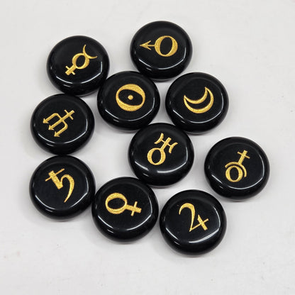 Nine round black stone pendants with gold celestial and astrological symbols, arranged in a cluster on a light gray background.