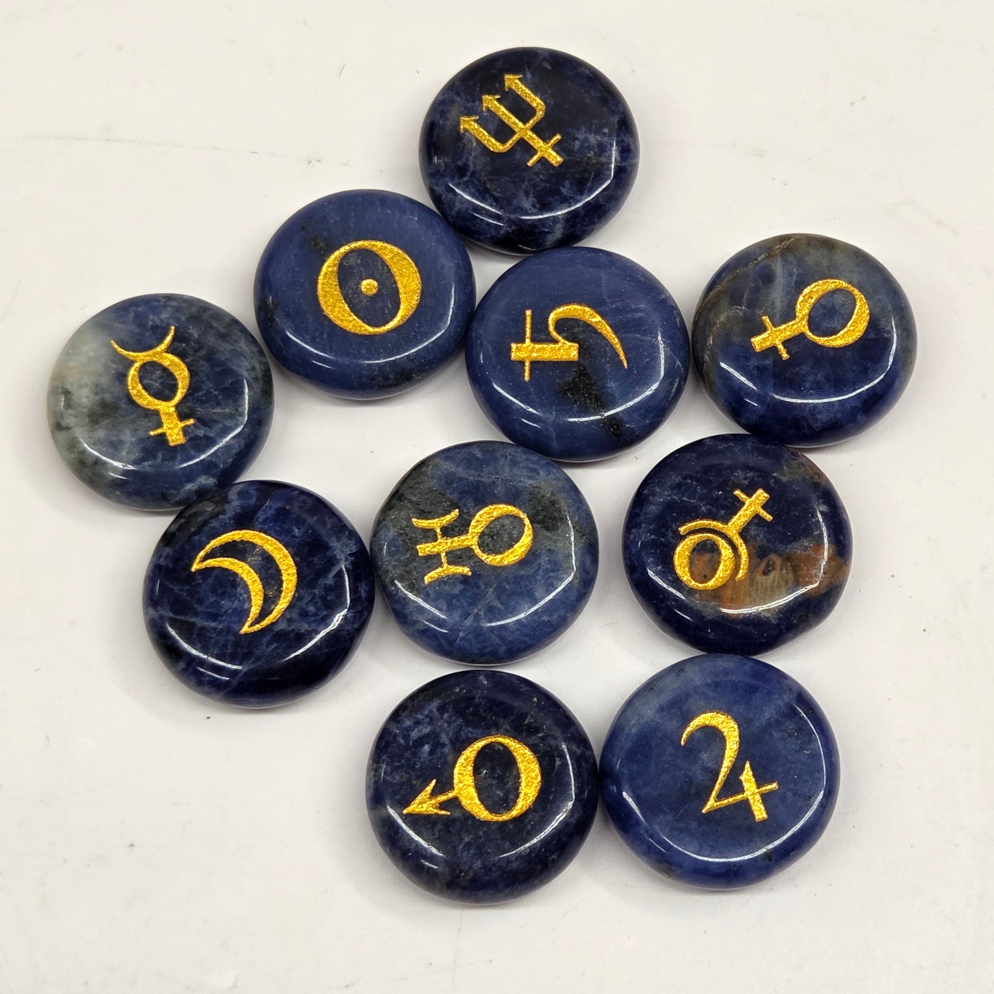 Nine polished dark blue selenite gemstone pendants with gold astrological symbols, arranged in a loose circle on a light off-white background.