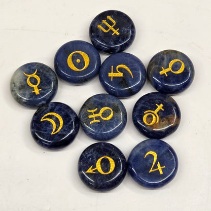 Nine polished dark blue selenite gemstone pendants with gold astrological symbols, arranged in a loose circle on a light off-white background.