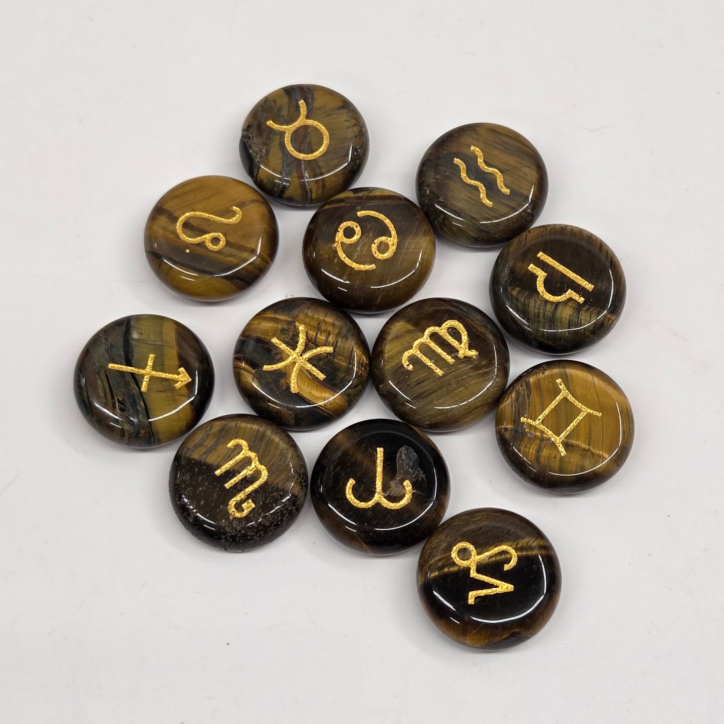 A set of ten polished round gemstone pendants with astrological symbols, featuring a dark brown and black tiger's eye pattern with gold-colored symbols, arranged on a plain white background.