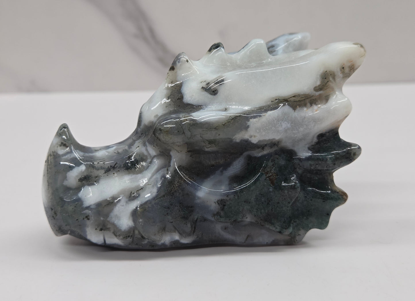 A carved stone sculpture of a dragon head, made from polished dark gray and white marbled stone, set against a light gray background.