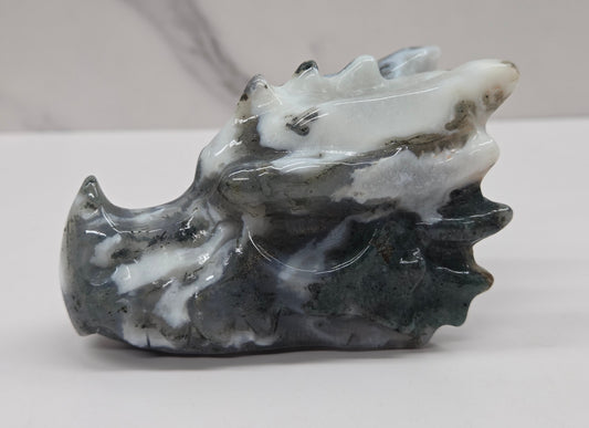 A carved stone sculpture of a dragon head, made from polished dark gray and white marbled stone, set against a light gray background.