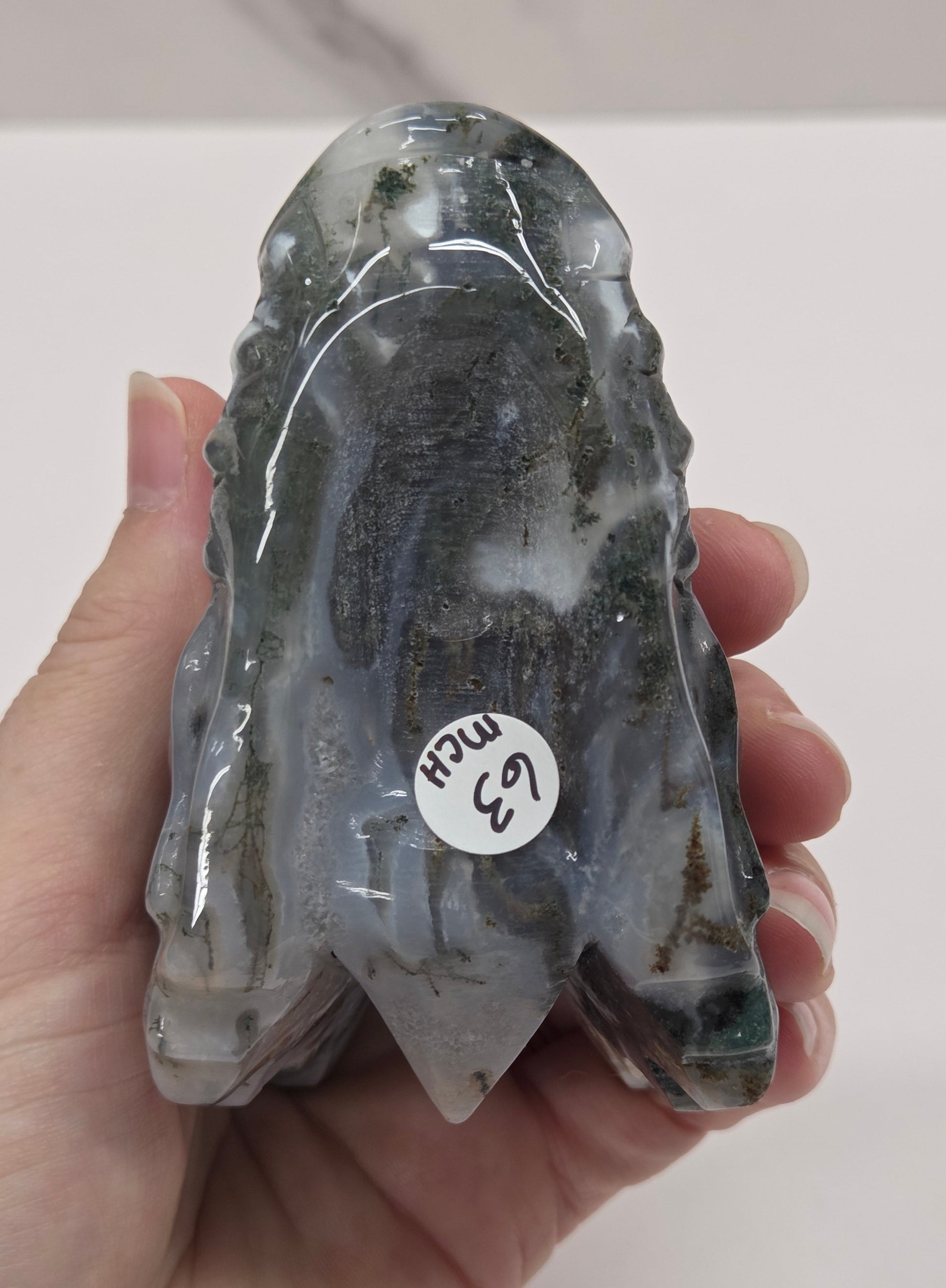 A hand holding a polished gray stone cluster with a small white sticker that reads '6.3 car'.