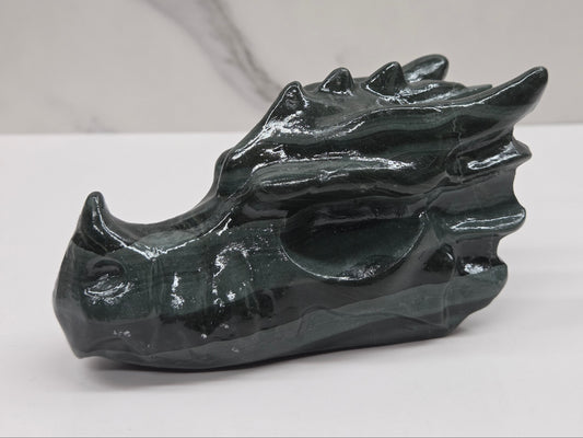A dark green polished stone dragon head sculpture, shown on a white surface with a light gray marble-patterned background.