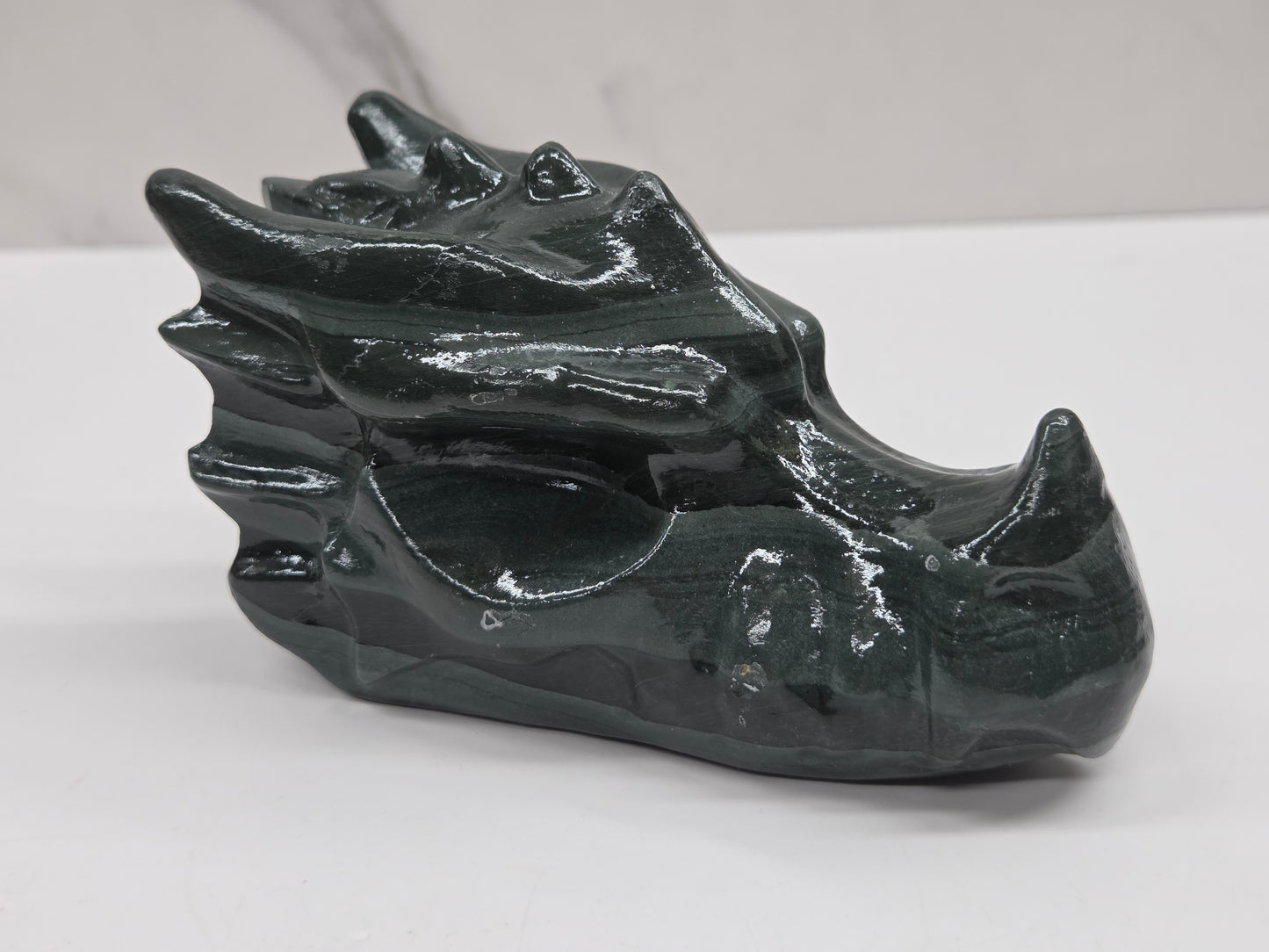 A glossy black dragon head figurine carved from polished stone, displayed on a light gray surface with a white marble background.