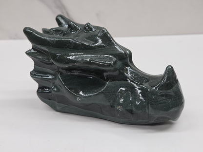 A glossy black dragon head figurine carved from polished stone, displayed on a light gray surface with a white marble background.
