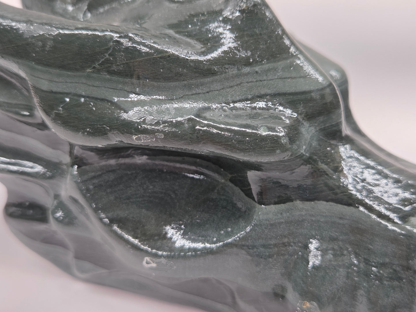 A close-up of a glossy dark gray stone sculpture with organic, flowing contours and reflective highlights on a plain light background.
