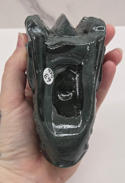A hand holding a glossy black ceramic vessel, likely a small planter or candle holder, with a small white sticker on the side.