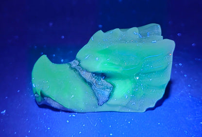 A translucent light green wax melt or solid perfume block with a textured, organic shape, photographed on a dark blue background under UV light.
