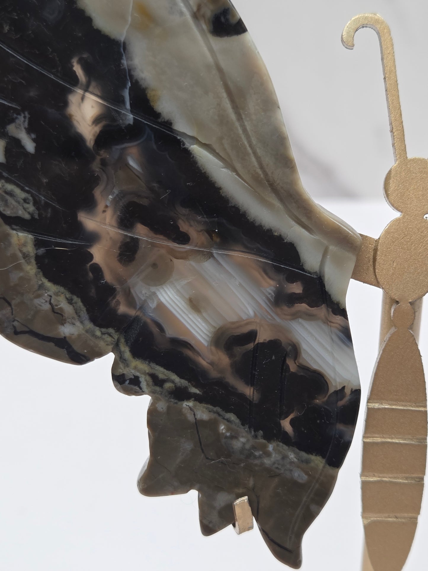 A close-up of a decorative hanging ornament featuring a stylized profile of a person in profile, made from polished black, gray, and beige agate-like stone, with a gold-toned metal hook at the top.