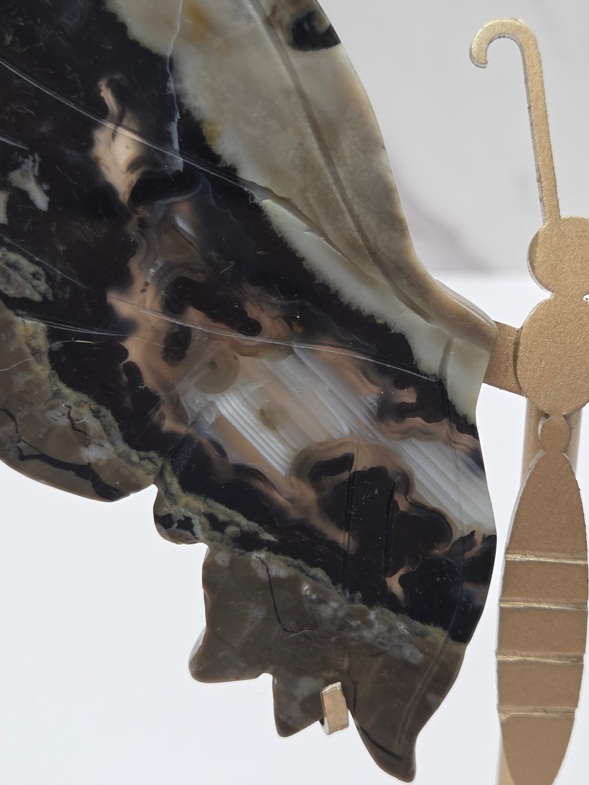 A close-up of a decorative hanging ornament featuring a stylized profile of a person in profile, made from polished black, gray, and beige agate-like stone, with a gold-toned metal hook at the top.