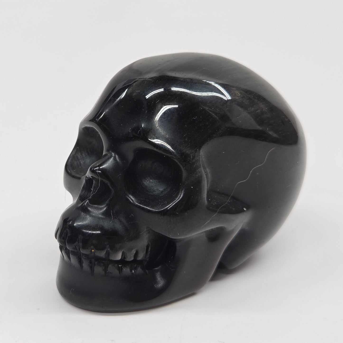 A polished black skull figurine, likely carved from obsidian or black stone, shown from a three-quarter angle against a plain white background.