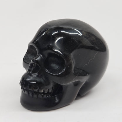 A polished black skull figurine, likely carved from obsidian or black stone, shown from a three-quarter angle against a plain white background.