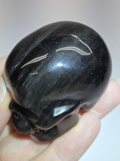 A hand holding a small, polished black skull-shaped stone or carving against a plain light background.