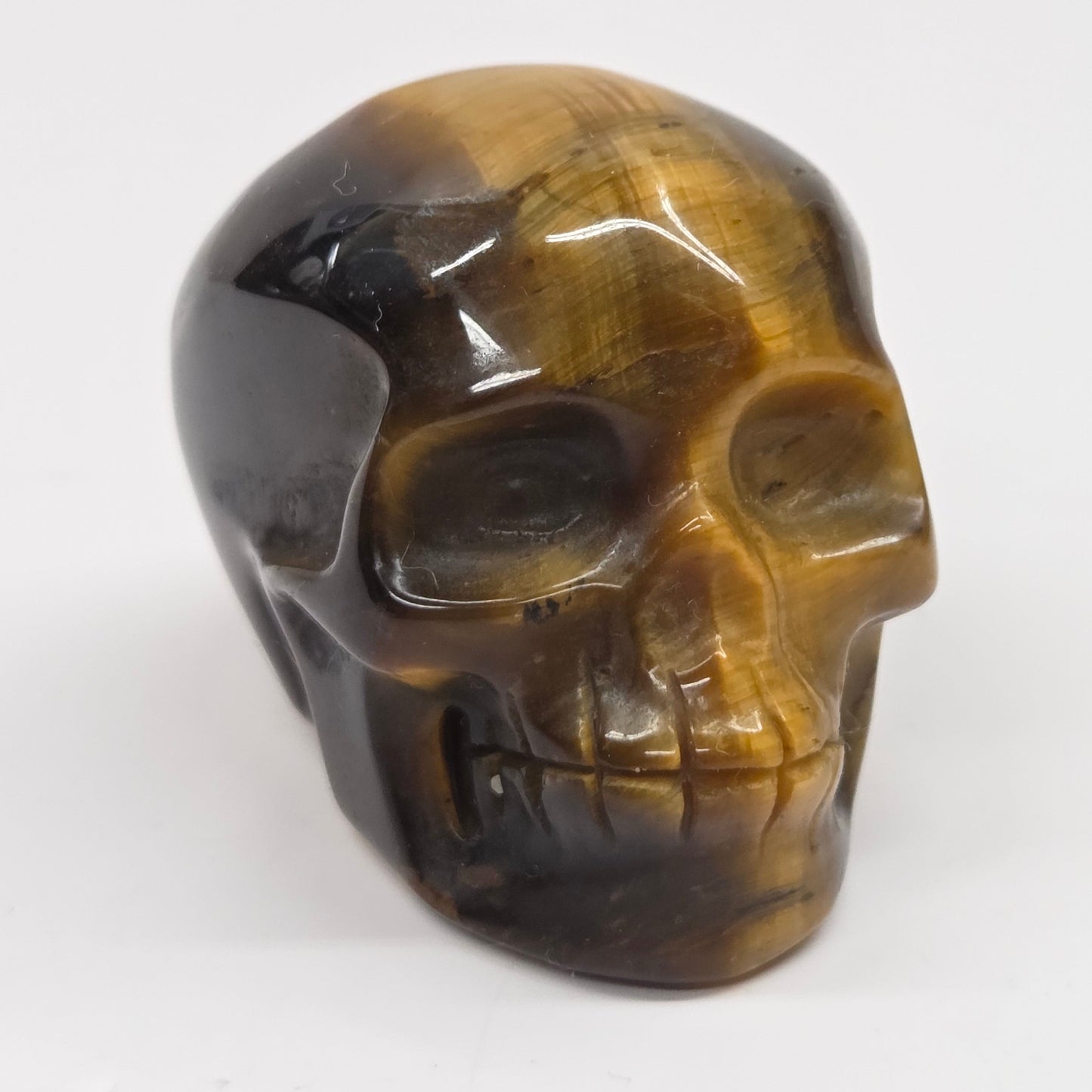A polished carved skull made of tiger's eye stone, showing natural brown and golden-yellow banded patterns, set against a plain white background.