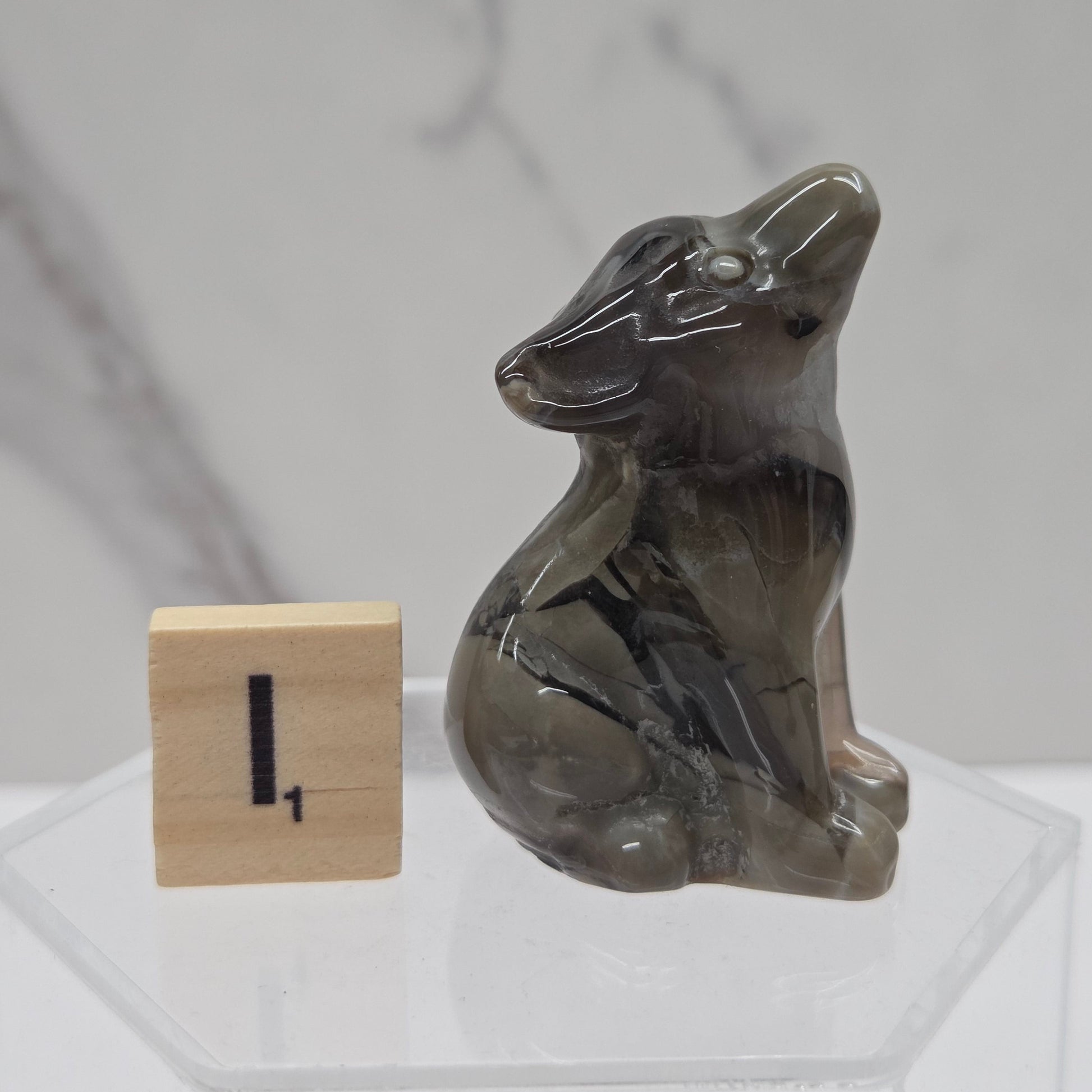 A small carved stone figurine of a seated rabbit, displayed on a clear acrylic stand next to a wooden block with the number 1, against a light gray marble-patterned background.