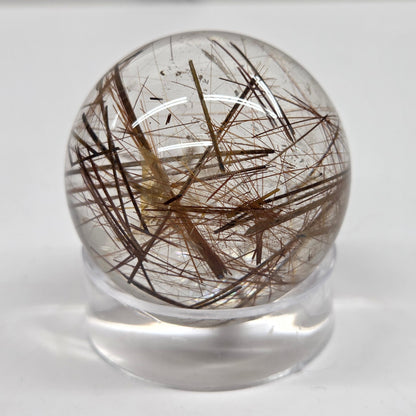 A clear glass or acrylic sphere containing numerous dark brown to black hair-like inclusions, displayed on a small clear stand against a plain light background.