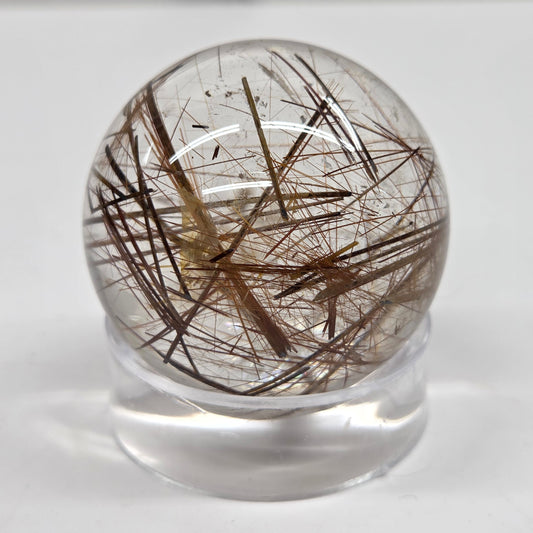 A clear glass or acrylic sphere containing numerous dark brown to black hair-like inclusions, displayed on a small clear stand against a plain light background.