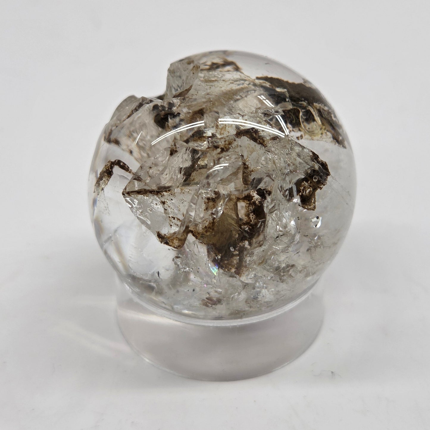 A clear glass sphere containing natural quartz crystals and metallic flecks, displayed on a small clear glass stand against a white background.