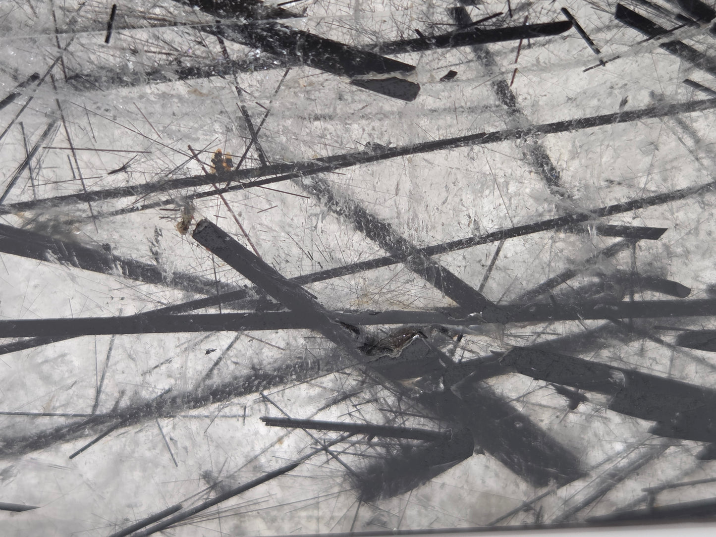 A close-up view of a scratched transparent surface with multiple dark linear marks and debris scattered across it.
