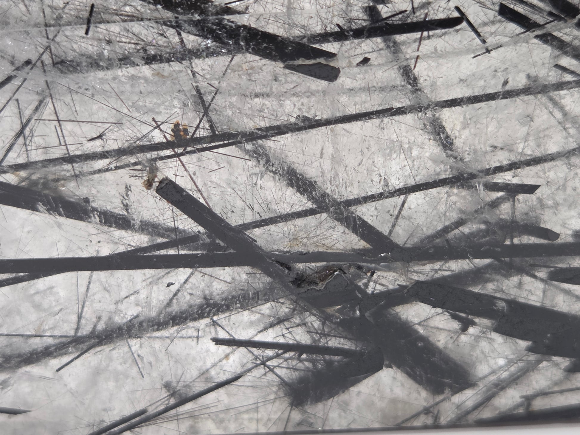 A close-up view of a scratched transparent surface with multiple dark linear marks and debris scattered across it.