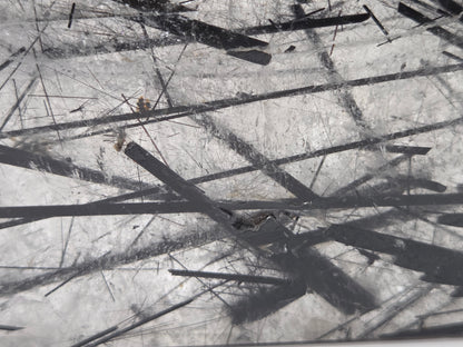 A close-up view of a scratched transparent surface with multiple dark linear marks and debris scattered across it.