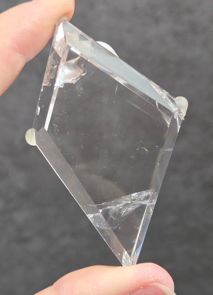 A hand holding a clear, geometric crystal block with sharp, faceted edges against a dark gray textured background.