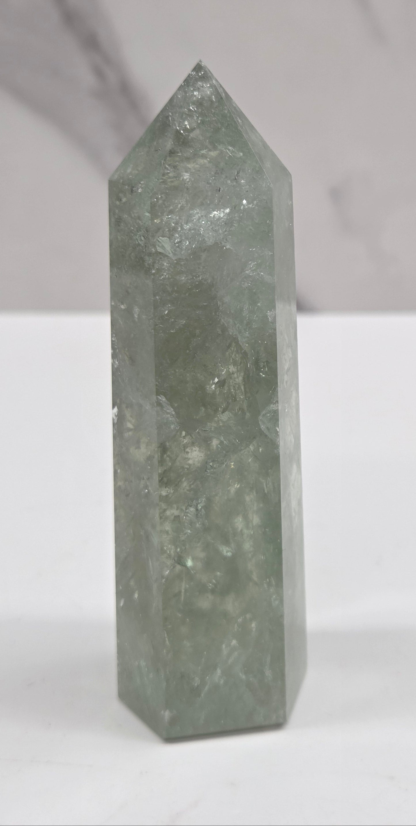A polished green crystal point displayed horizontally against a split white and light gray marble background.