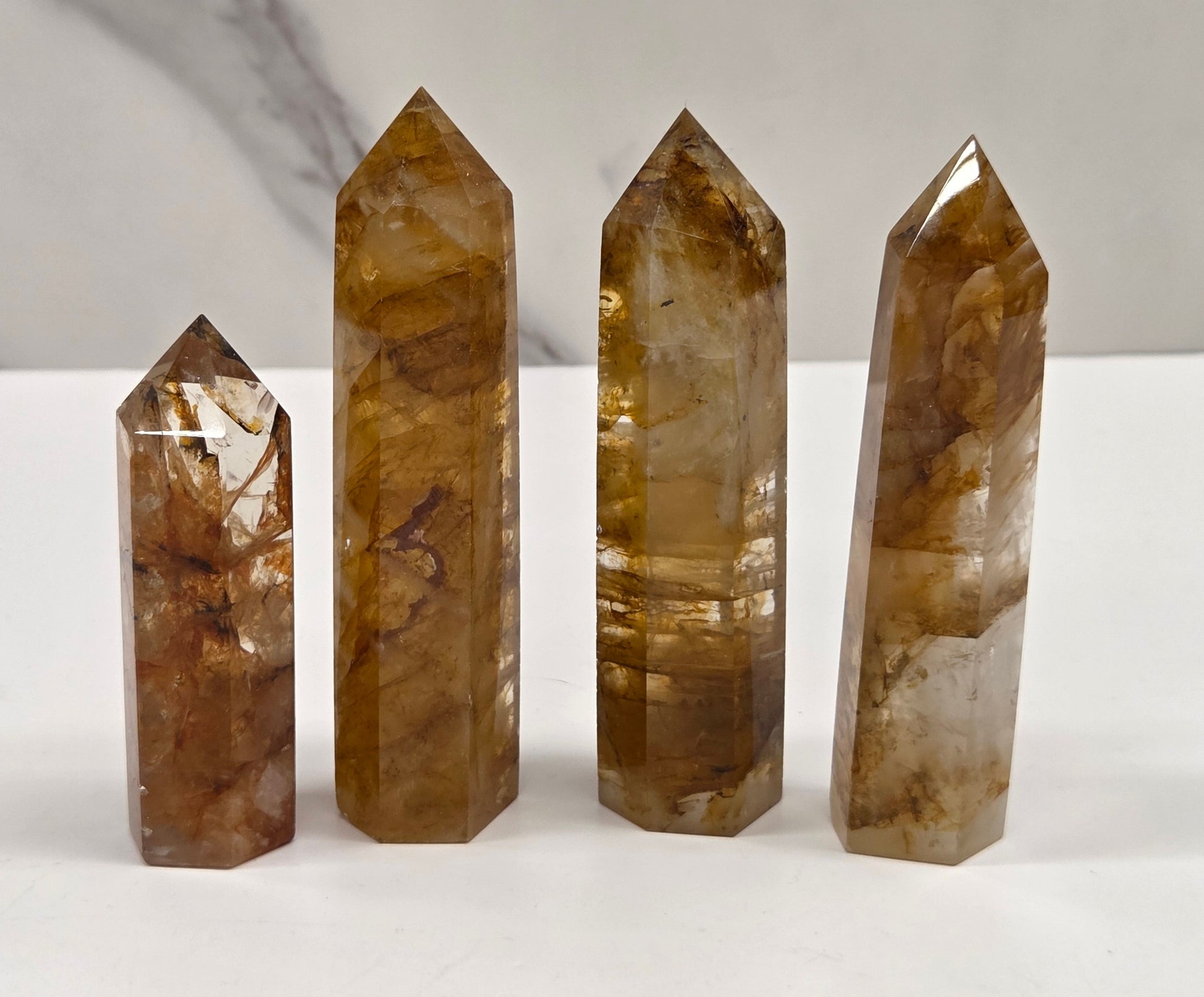 Four polished brown and amber-toned crystal points of varying heights arranged in ascending size order on a white surface with a light gray marble-look background.