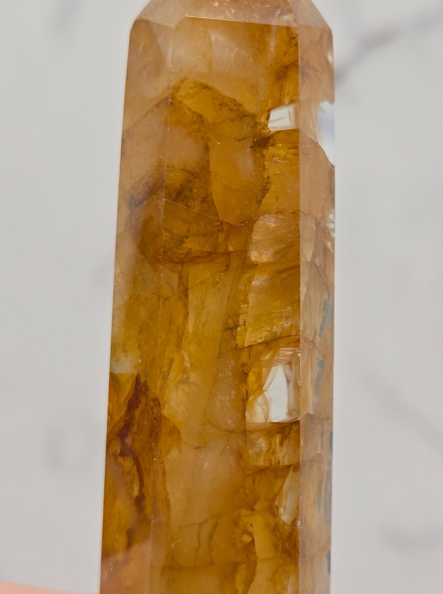 A close-up of a faceted golden-yellow crystal point held by a finger against a light marble background.
