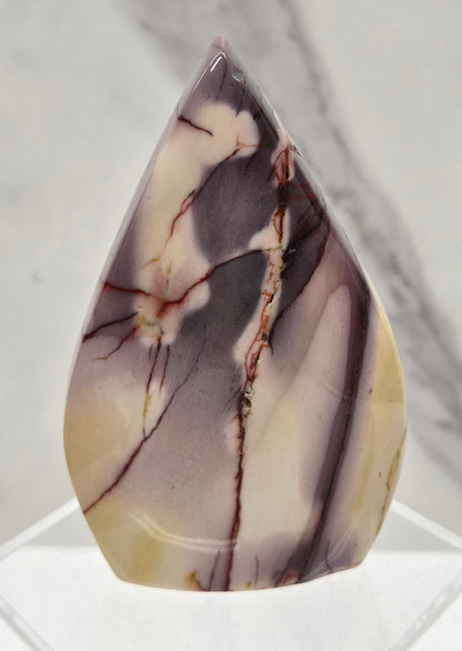 A polished teardrop-shaped gemstone with a marbled pattern of gray, cream, and brown veins, displayed on a clear acrylic stand against a light gray marble background.