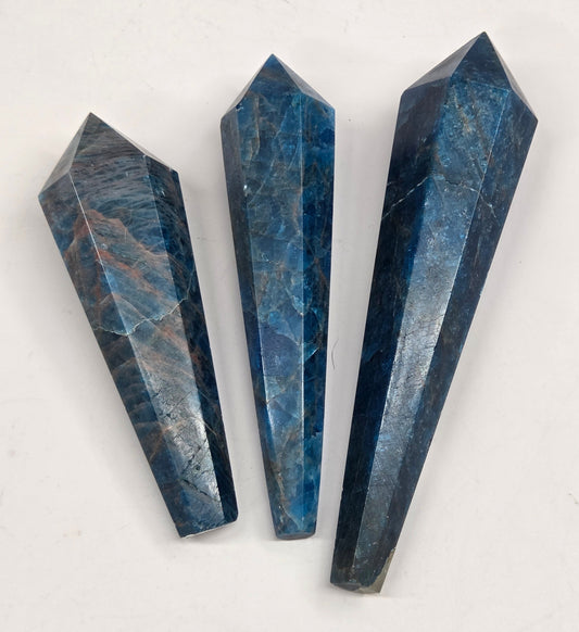 Three faceted blue stone crystal points arranged vertically on a plain off-white background.