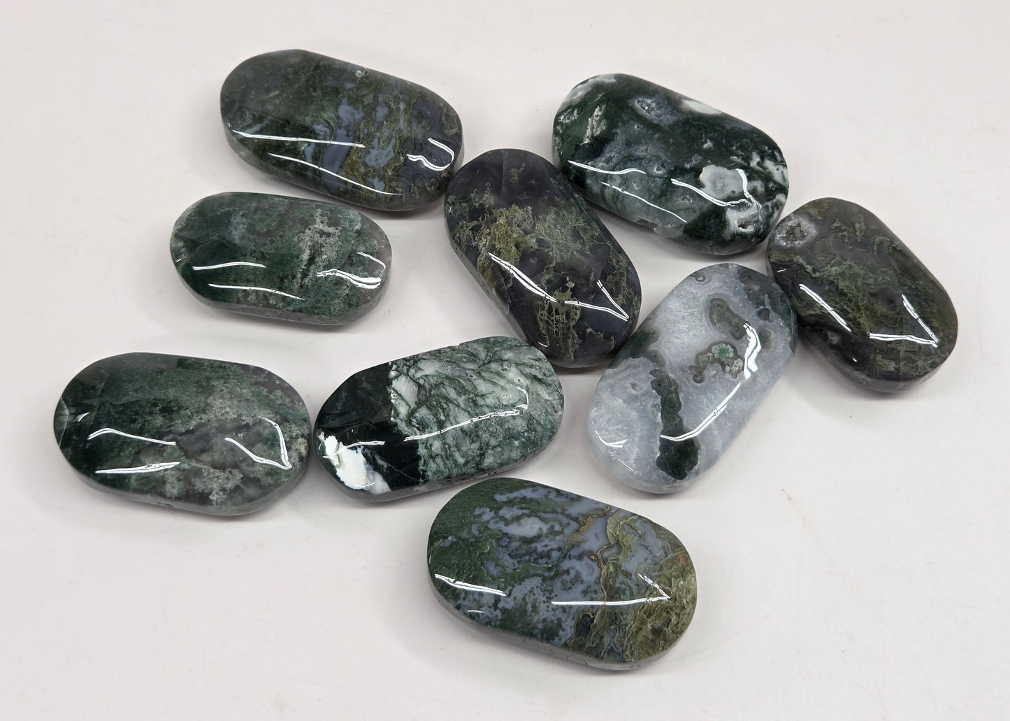 A group of nine polished dark green and gray tumbled stone beads with natural marbled patterns, arranged on a plain white surface.