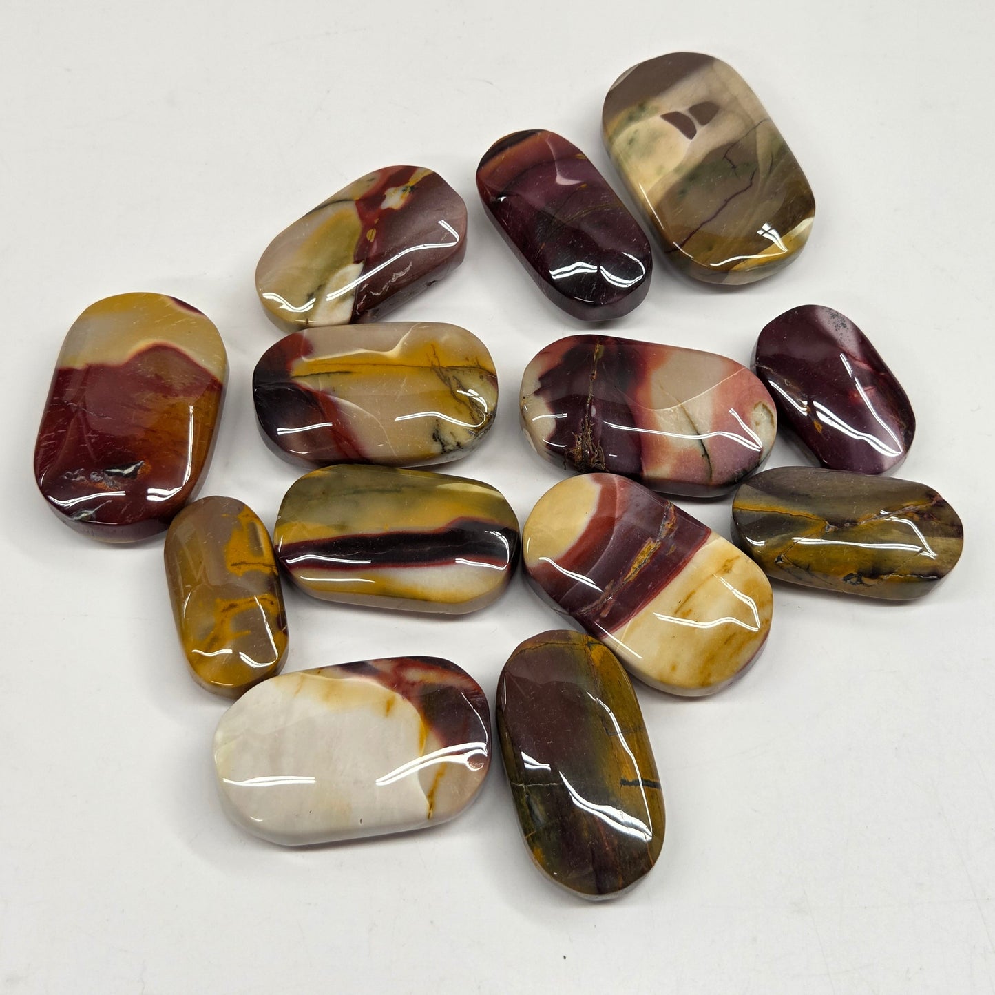 A group of polished tumbled gemstone pucks with natural marbled patterns in brown, gold, purple, and cream, arranged on a plain white background.
