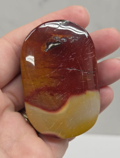 A hand holding a polished, rounded stone with a marbled pattern of deep reddish-brown and translucent yellow.