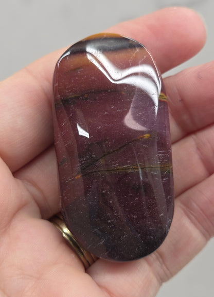 A polished reddish-brown gemstone with gold and dark brown veining, held in a person's hand.