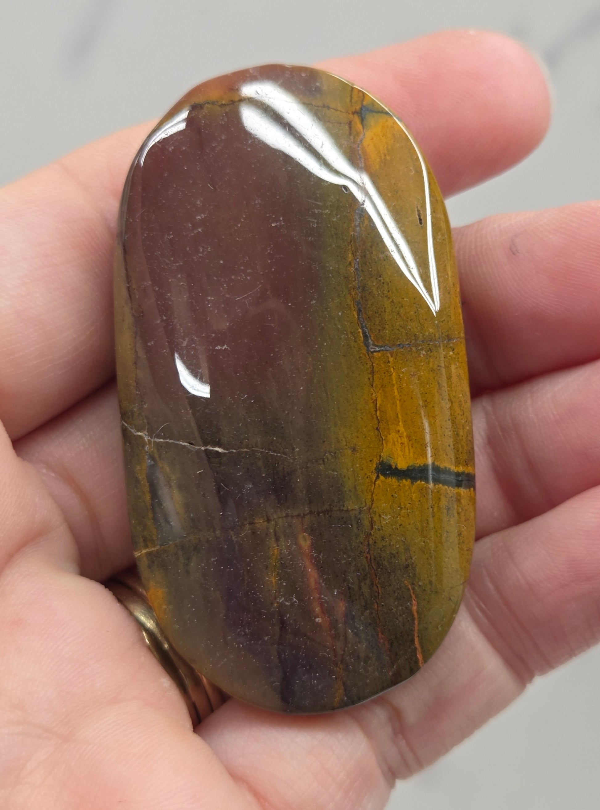 A polished brown and yellow stone held in a person's hand against a light gray marble background.