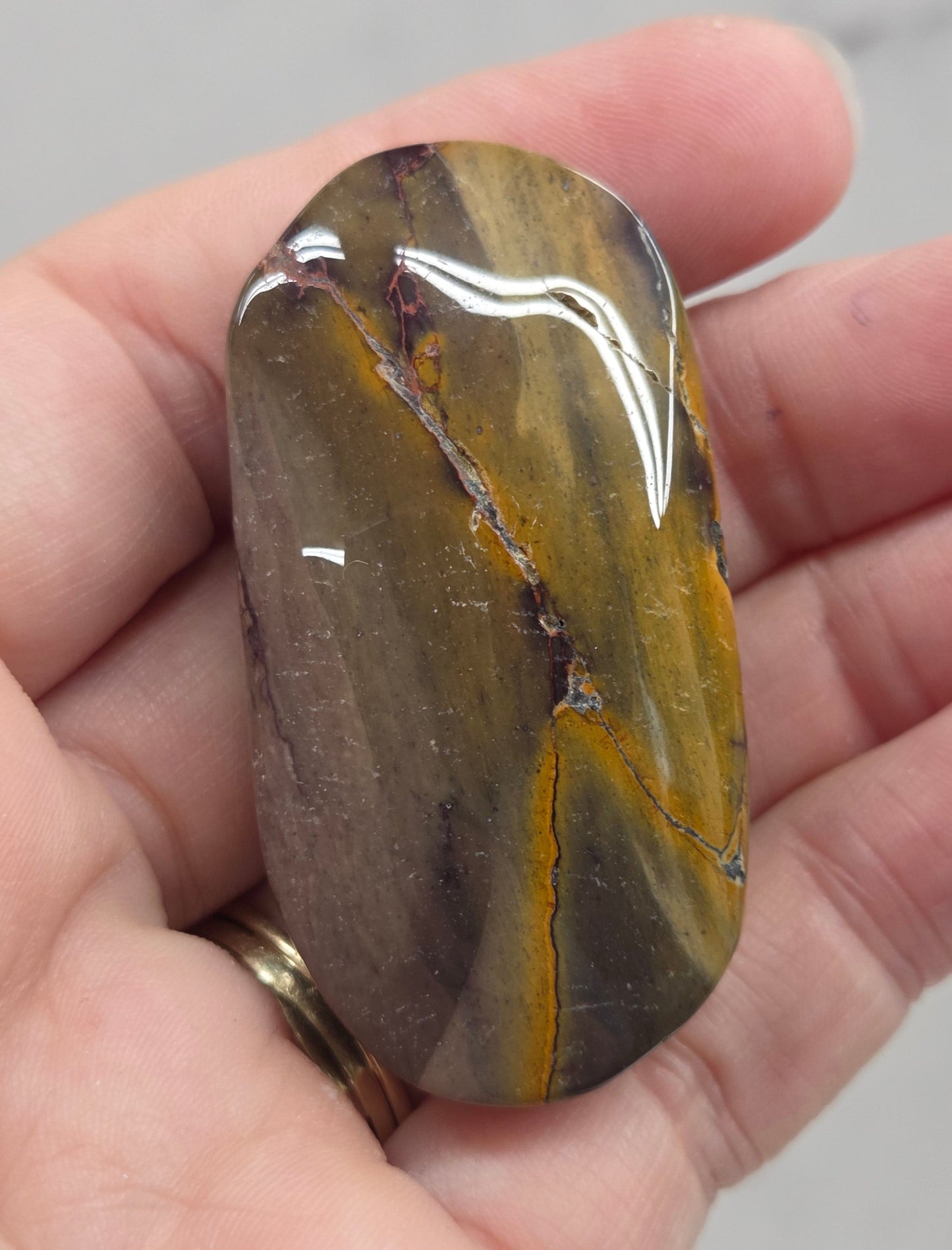 A polished natural stone with yellow, brown, and gray banded patterns, held in a person's hand.