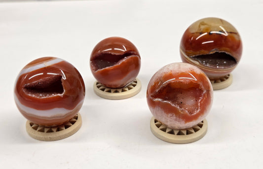 Four polished agate stone spheres with natural banding, each displayed on a small round wooden stand, arranged on a white surface.