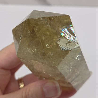 A faceted natural quartz crystal held in a person's hand against a white background.