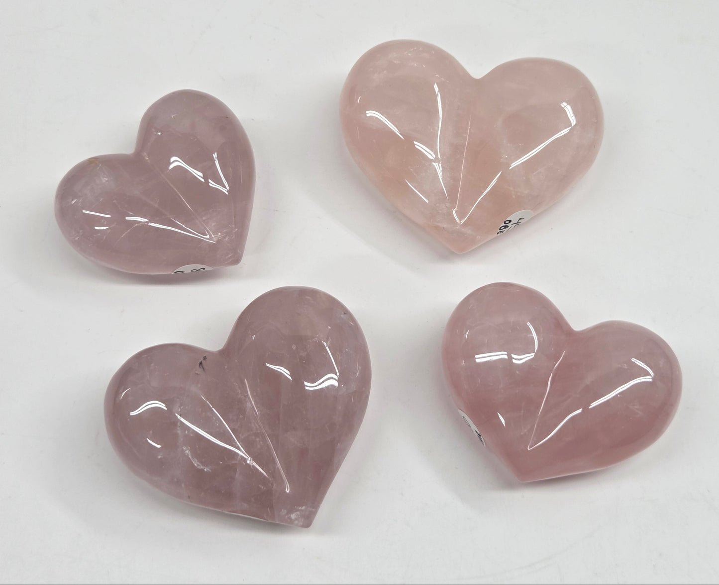 Four polished heart-shaped rose quartz gemstones in varying shades of dusty pink and lavender, arranged on a plain white background.
