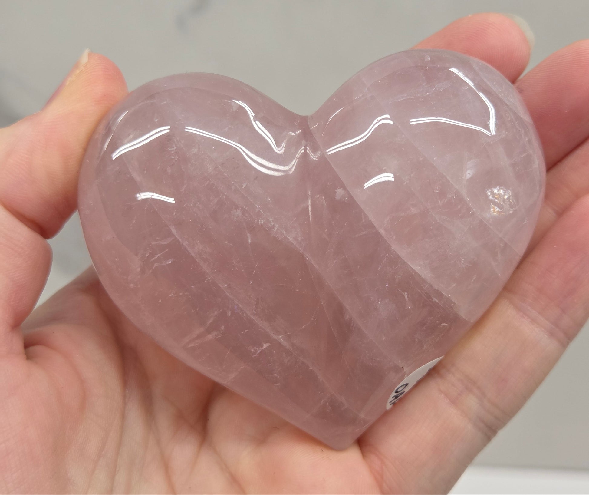 A hand holding a polished, heart-shaped rose quartz crystal.
