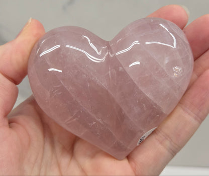 A hand holding a polished, heart-shaped rose quartz crystal.
