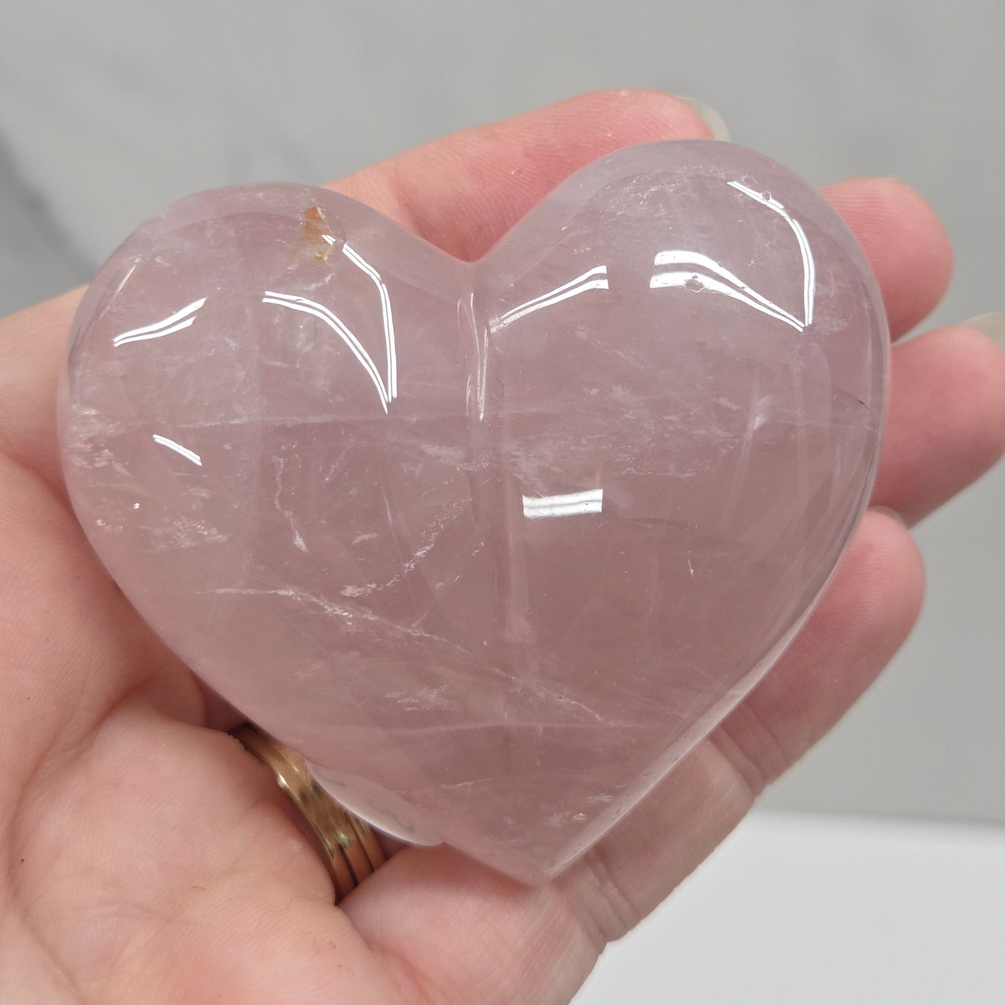 A hand holding a polished rose quartz heart-shaped crystal against a light gray marble background.