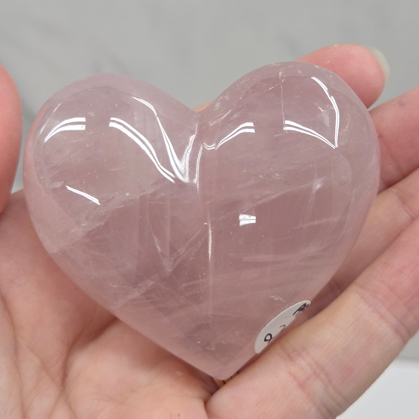 A translucent pink heart-shaped crystal ornament held in a person's hand against a light gray marble-like background.