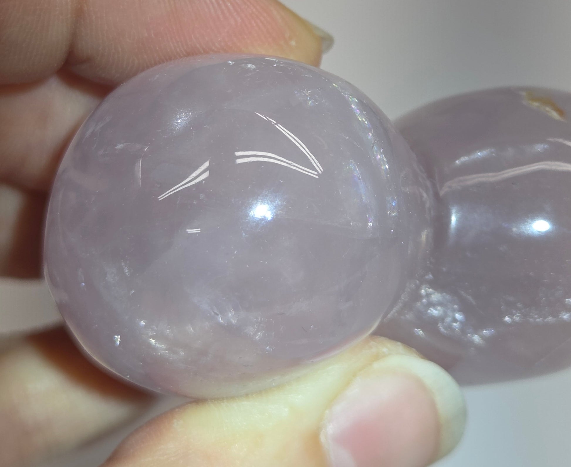 A close-up of a person holding a double-gourd-shaped carved stone pendant made of pale lavender quartzite, showing its smooth, polished texture and natural inclusions.