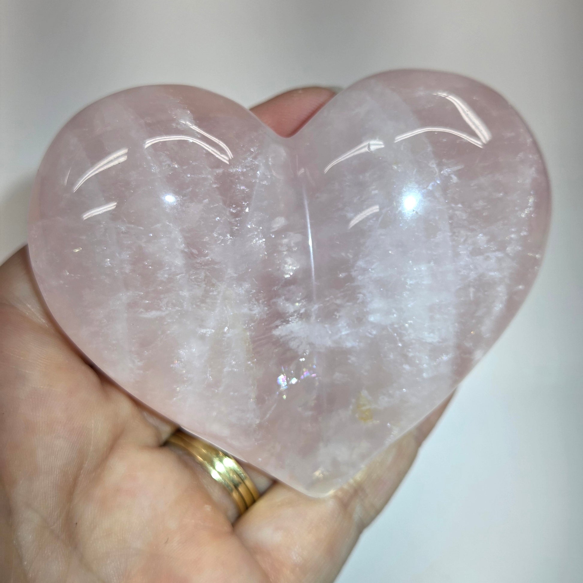 A heart-shaped rose quartz crystal wand being held in a hand, showing its smooth, polished texture and light pink color.