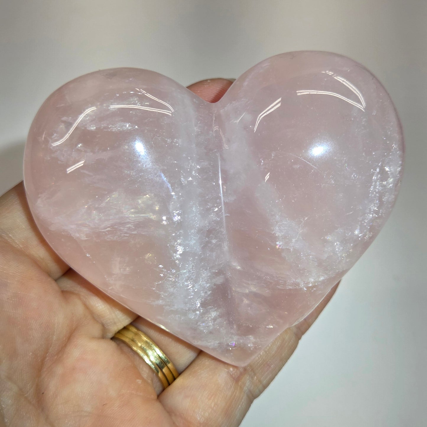 A heart-shaped rose quartz crystal held in a person's hand, showing its soft pink color and natural cloudy texture.