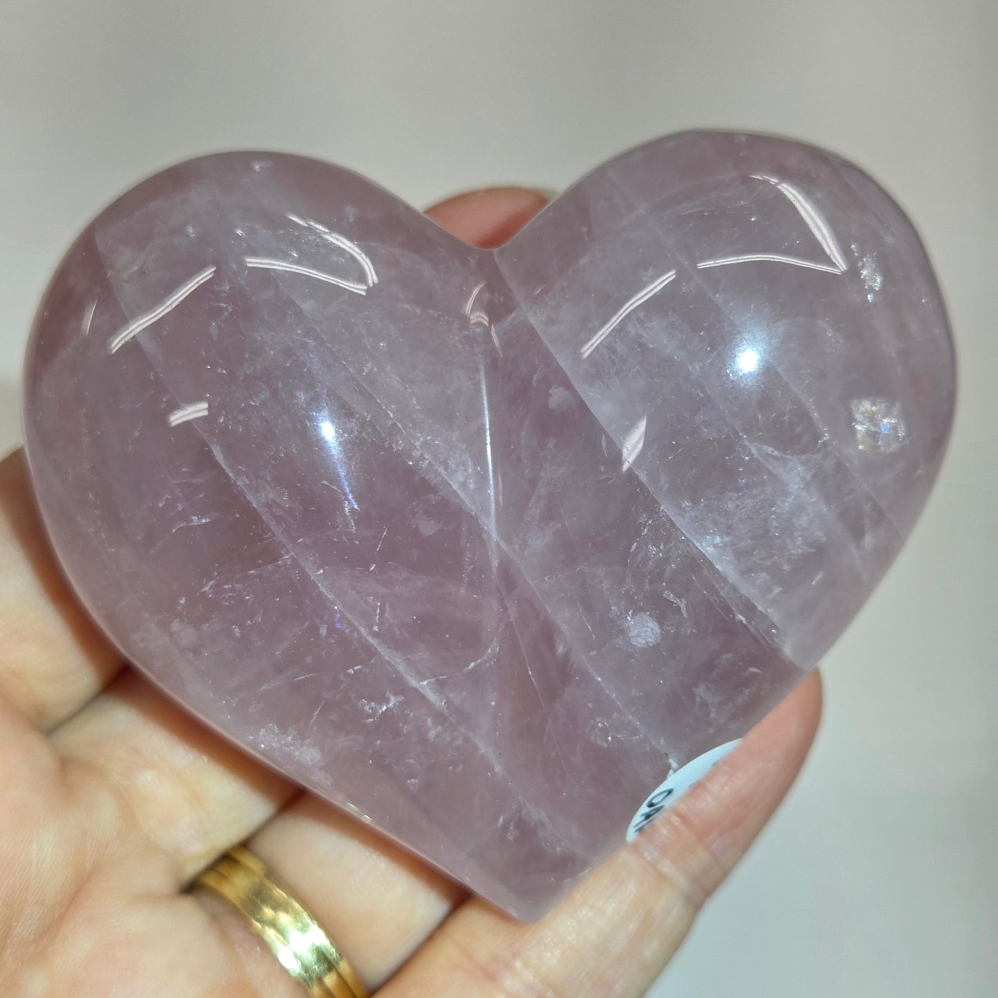 A heart-shaped rose quartz crystal ball held in a person's hand, showing its smooth, polished surface and natural lavender-purple color.